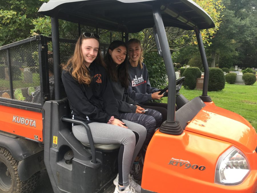 Seniors Casey Dagostino and Emma Mckee and sophomore Isabelle Magré ride a landscaping cart at the Newton Cemetery for their volunteer project. 