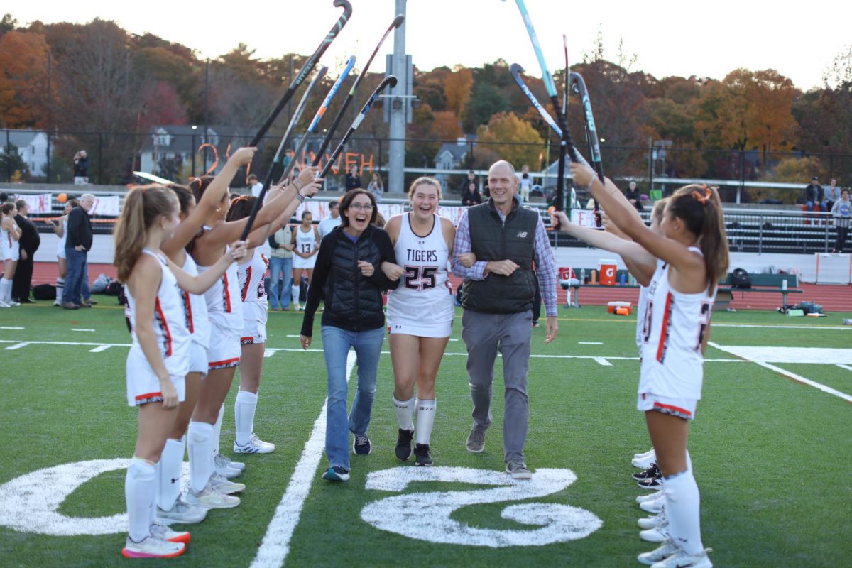 Senior Meghan Devaney, accompanied by her parents, walks across the turf during pre-game senior celebrations Thursday, Oct. 24. 