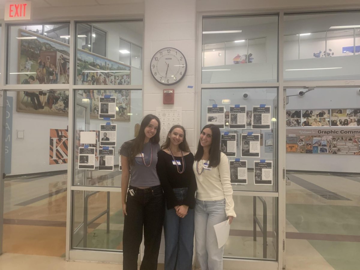 Seniors Maya Solomon, Shaelyn Shields and junior Kayleigh Shields stand beside candidates' photos during their League of Women Voters event, Saturday, Oct. 4. 